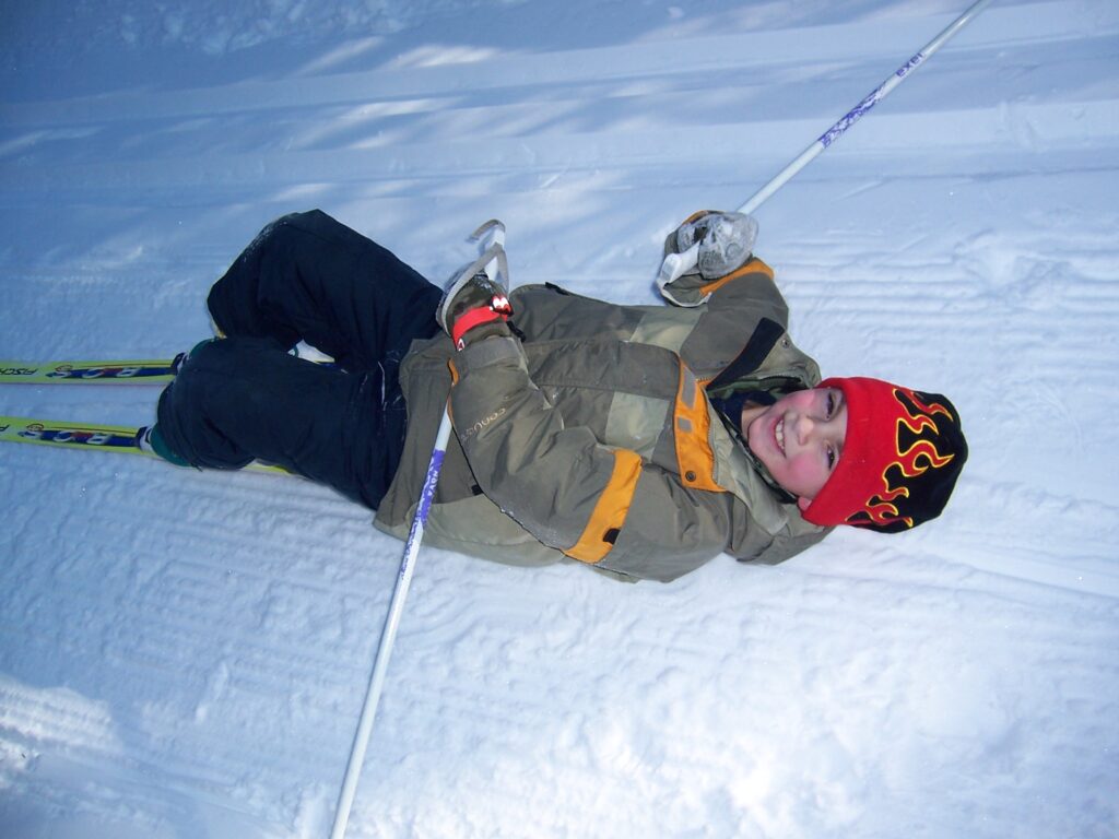 little boy on the snowy ground with cross country skis on