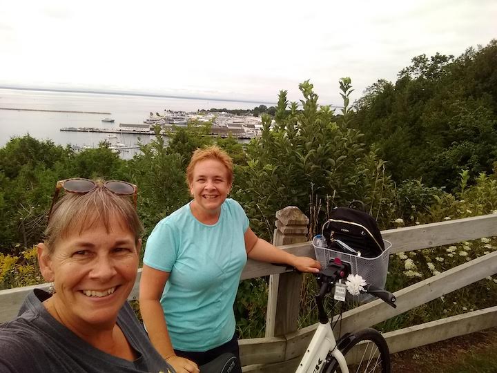 two women with bikes on top of hill overlooking macinac city