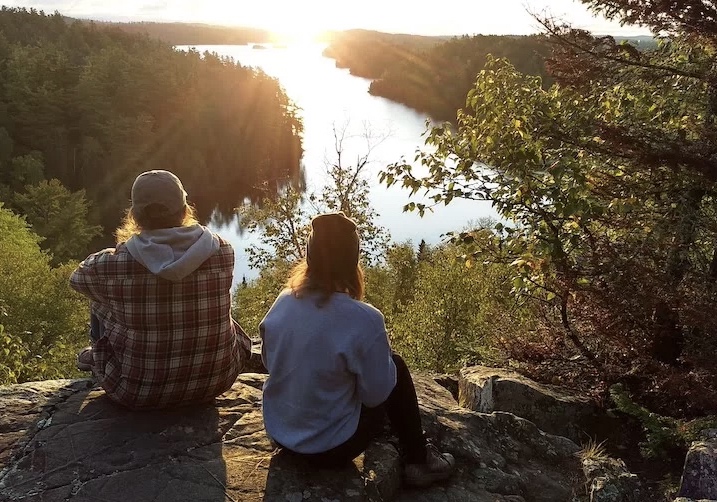 two women sit on a rock overlooking a lake at sunrise