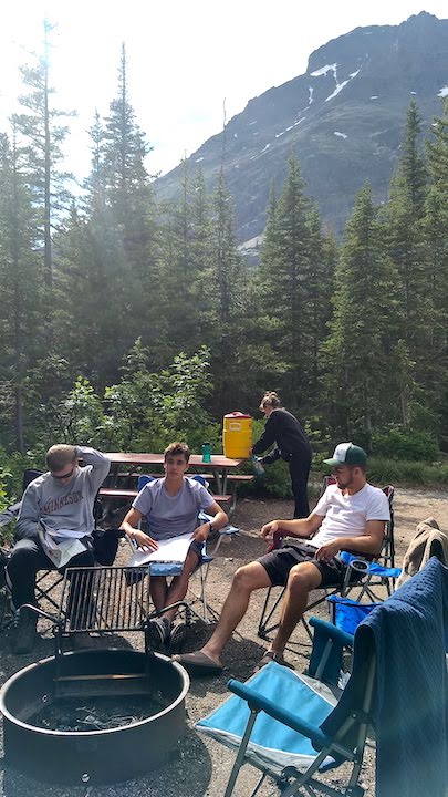 4 people relaxing at their campsite with a mountain in the background