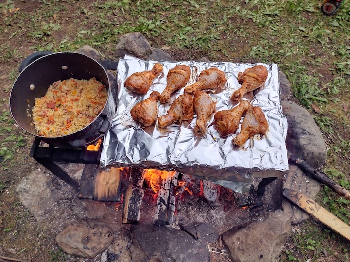 chicken legs and a pot of rice cooking over a campfire