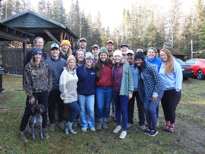 Group of adults plus one dog outside up north—woodcutting crew