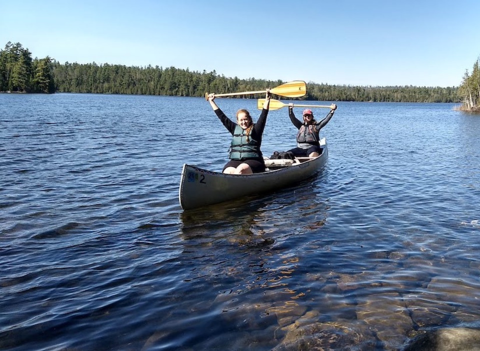 two women canoeing with paddles overhead