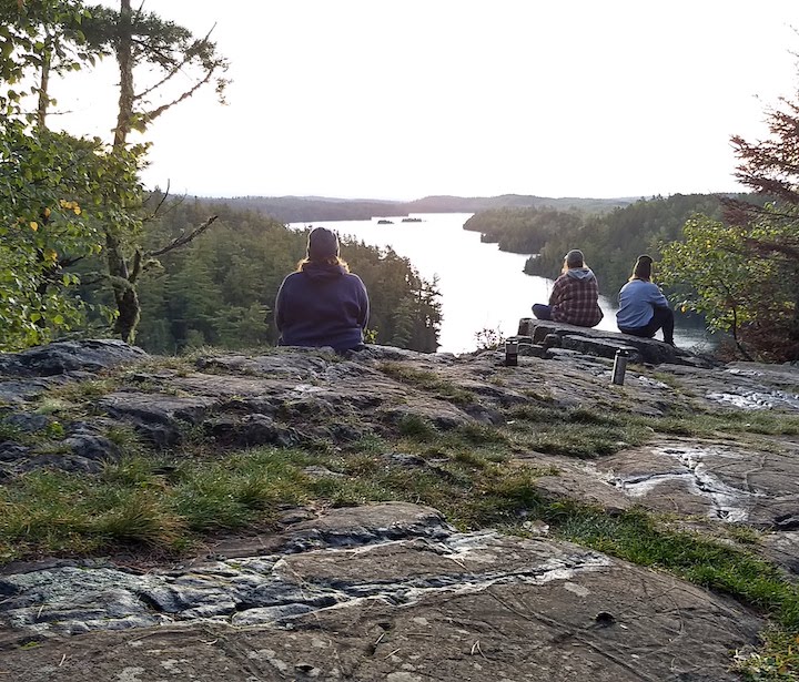 three women sit overlooking a long lake and the hills