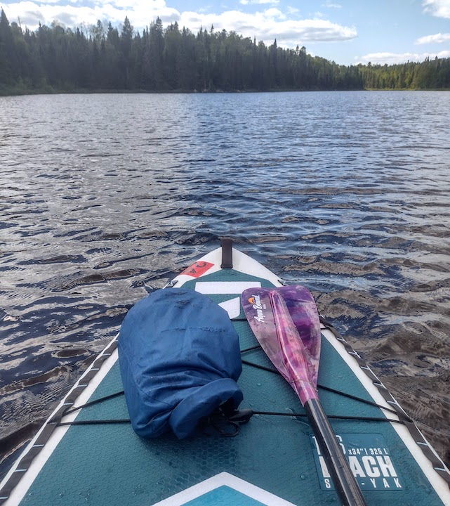 paddleboard on a lake, with paddle and dry bag