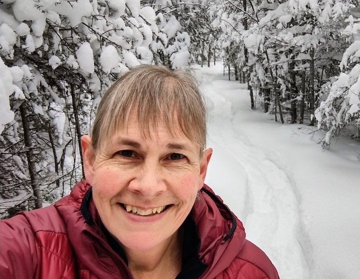 Sharon Brodin on a Minnesota snowshoe trail with snowy trees along the path