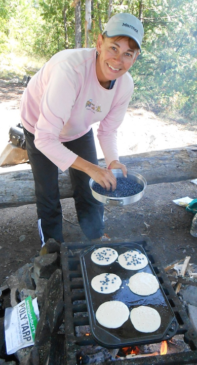 woman cooking blueberry pancakes over a campfire 