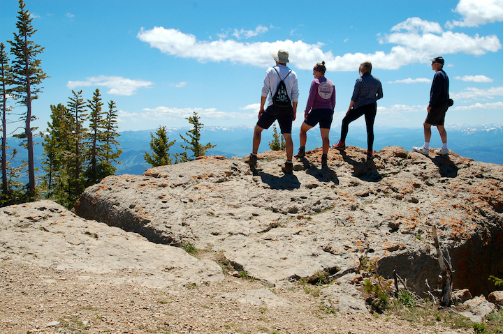 4 adults standing on a mountain top, overlooking more mountains