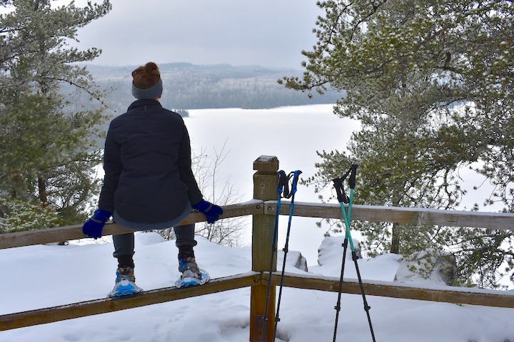 snowshoer sitting on a fence overlooking a frozen lake