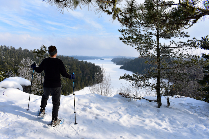 snowshoer with modern snowshoes and poles, overlooking a frozen lake
