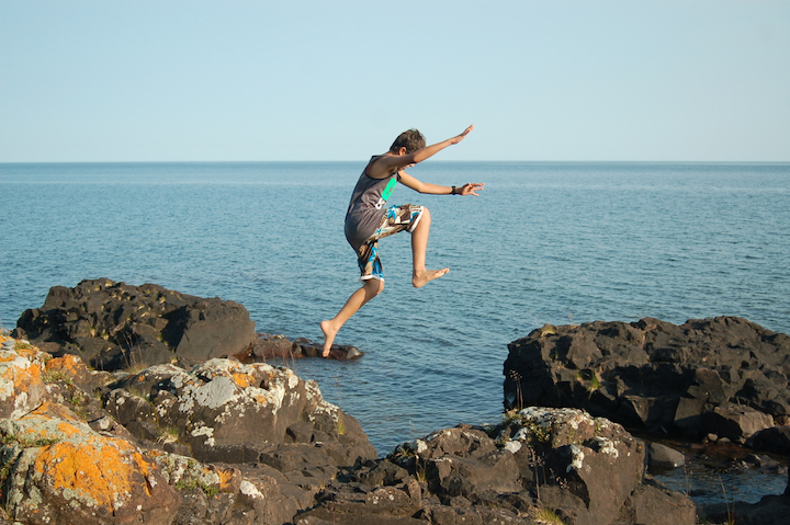 young boy jumping from one rock to another next to Lake Superior