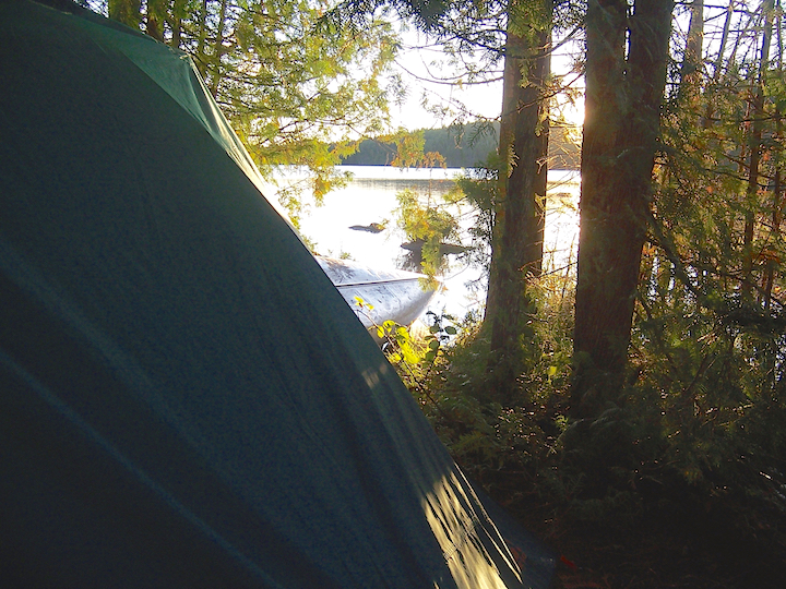 Looking out to a lake at sunrise, beside a tent with a canoe on-shore