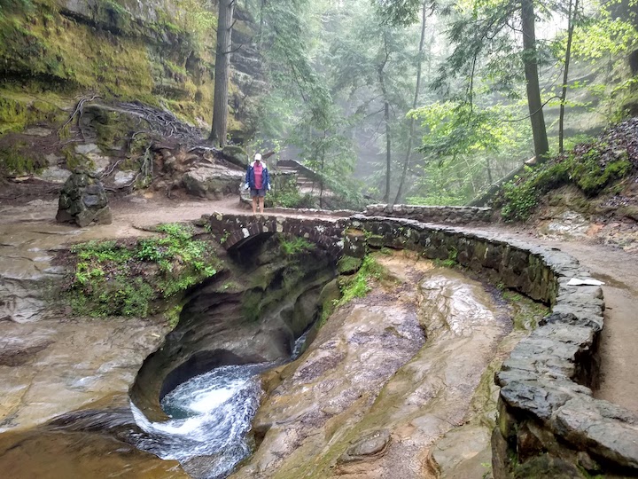 woman looking down into Devil's Bathtub in the creek, Hocking Hills