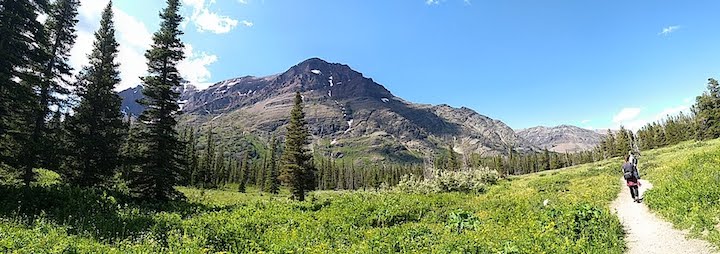 panorama of mountain meadow, two hikers on trail