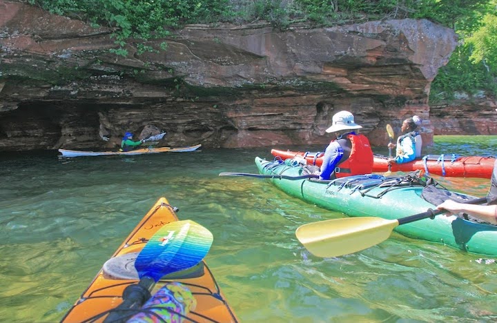 a group of kayakers relies on a guide through some sea caves