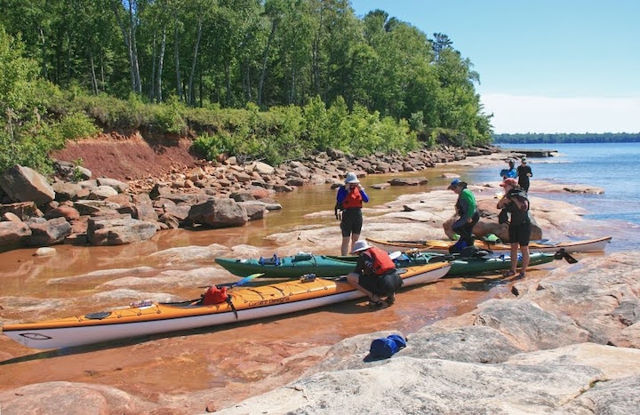 five women and their sea kayaks pulled up on a smooth rocky shoreline