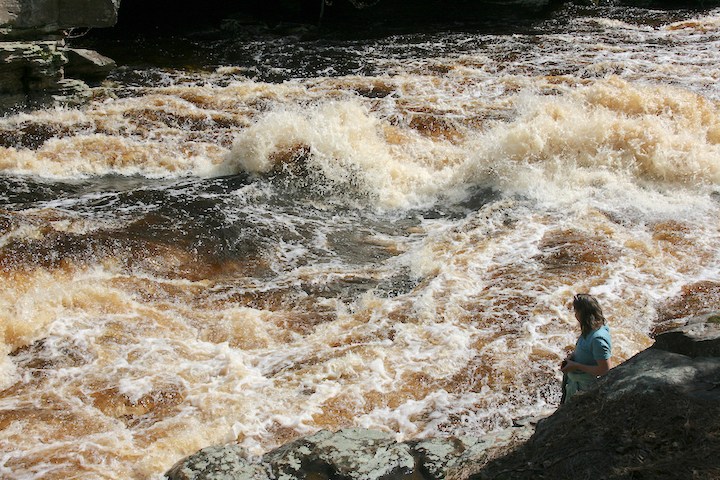 woman stands next to foaming river rapids