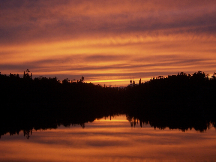 A blaze orange sunset over a tree-lined lake