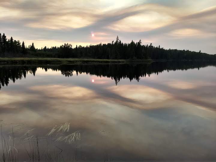 unique clouds are reflected on a lake's surface, with a tree-lined shore