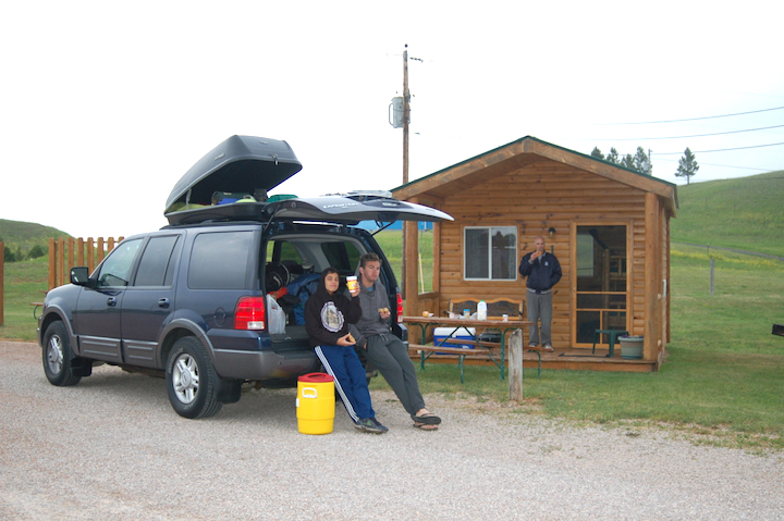 two boys by their truck and man standing on the front step of a camping cabin