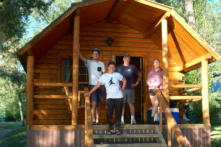 four adults stand on the porch of a log camping cabin