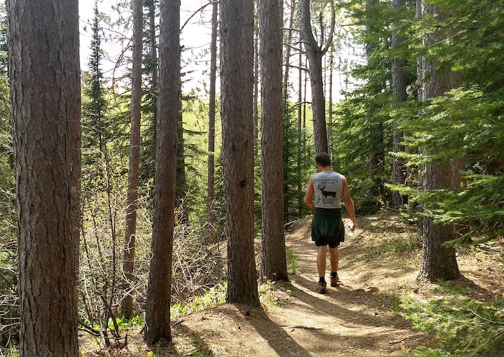 man hikes a narrow trail through tall trees