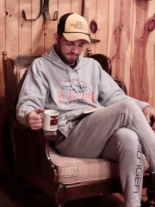man sitting in a chair reading his Bible and drinking coffee