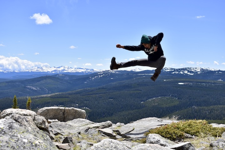 young man doing a high karate kick in front of the mountain views