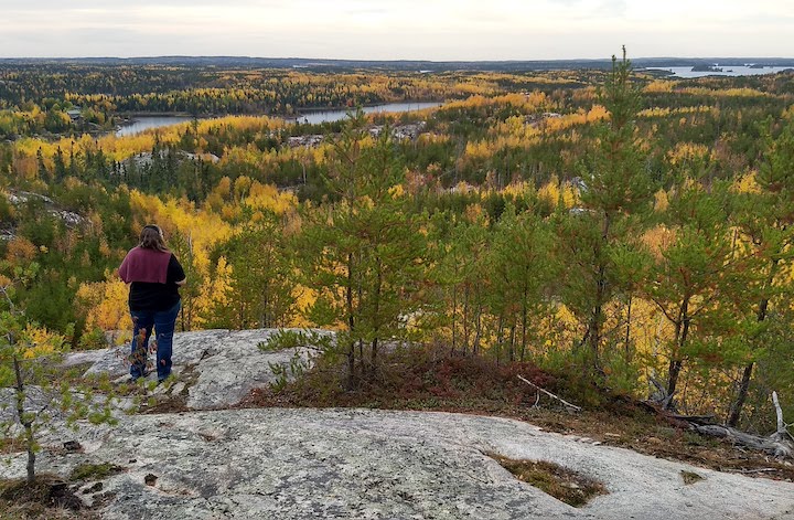 hiker at the top of a high hill overlooking fall colors and a lake below