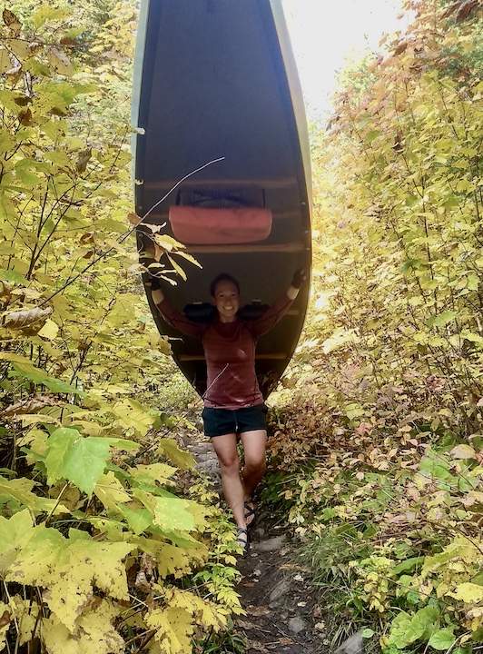 the author portages a canoe along a hilly trail in the woods