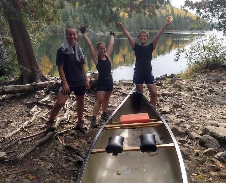 three women celebrate the end of a long portage in the Boundary Waters with one of their canoes