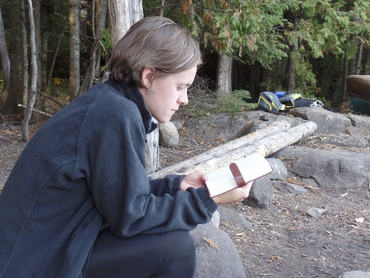 young woman reads her Bible in a canoe campsite