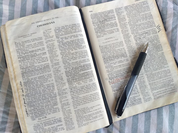 A Bible open to Colossians with a pen laying across the pages