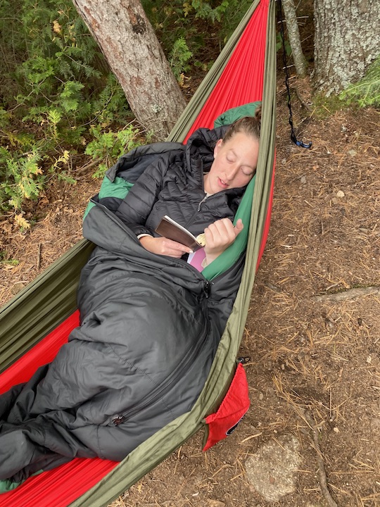woman reads her Bible while laying in a hammock in the campsite