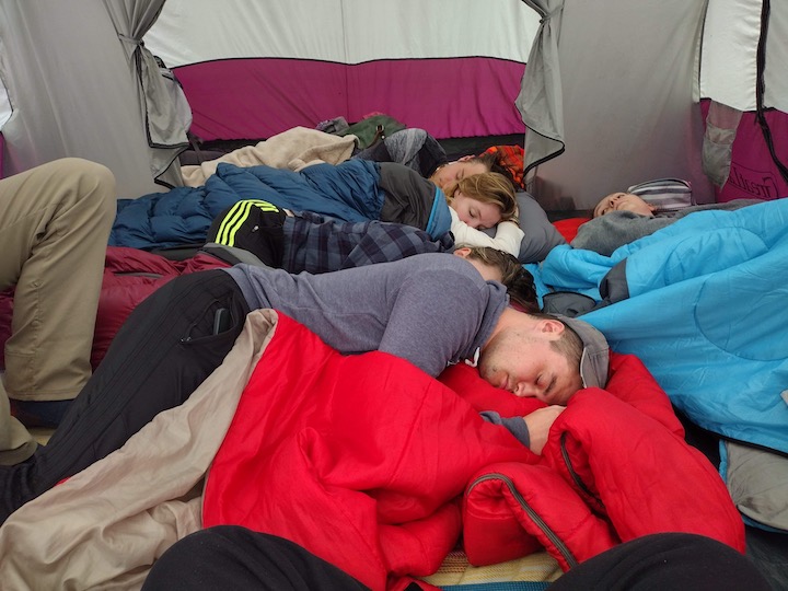a crowd of young adults napping in a tent during the day.
