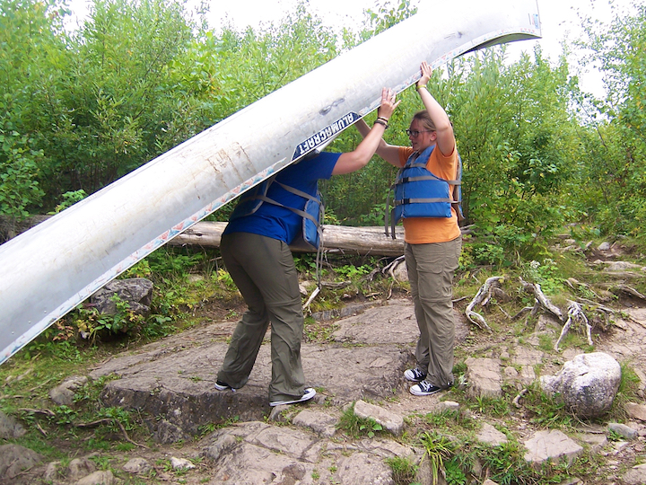 one woman holds the canoe bow while the other gets ready to lift it for portaging