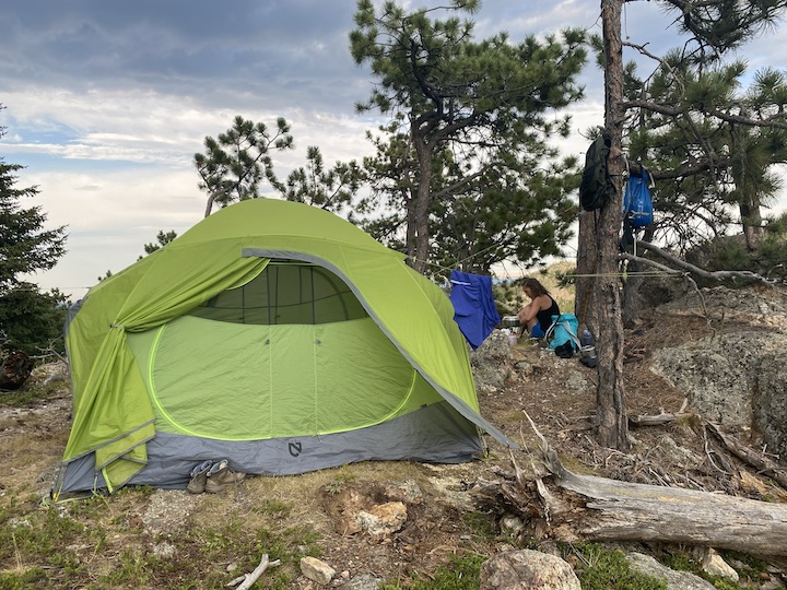 green tent on a mountain hillside, woman jut behind it