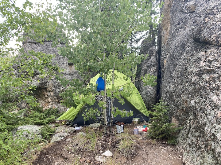 a small tent set up in a treed nook next to large rock formations