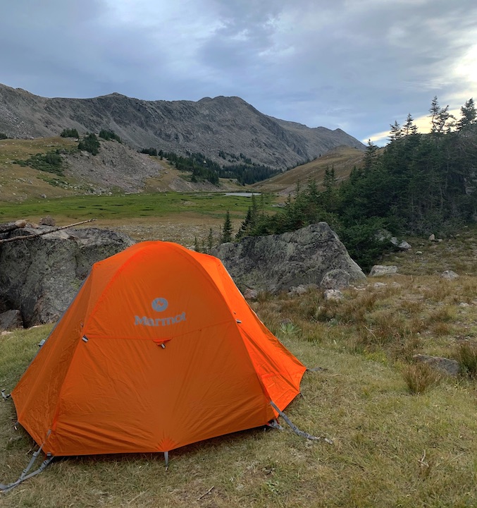 bright orange tent set up on a mountain with few trees around