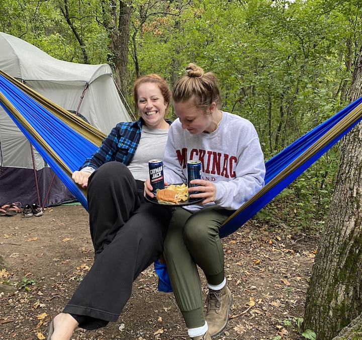 2 young women share a hammock at a campsite