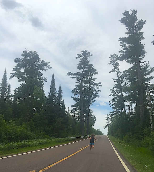 the author runs barefoot on a road surrounding by towering pine trees