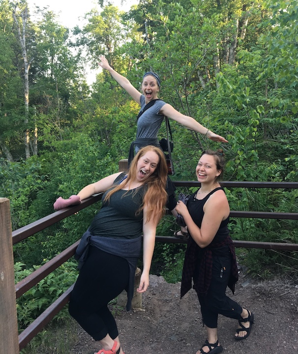 three young women on a hike in the woods, smiling and laughing