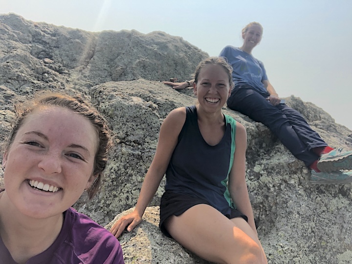 three women sit on a huge rock, smiling