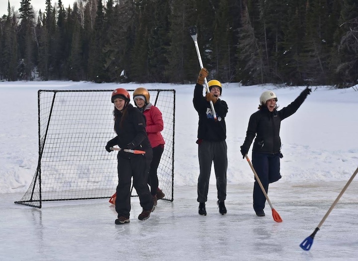 four women play broomball on a frozen lake