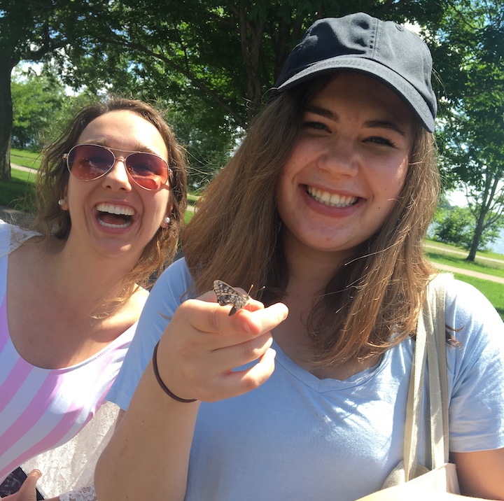 two young women laughing at a butterfly sitting on one's hand