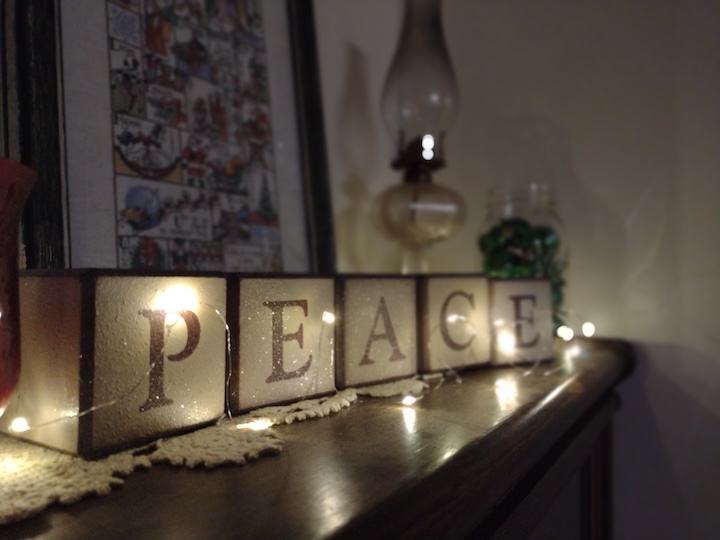 fairy lights illuminate blocks that spell "PEACE" sitting on a shelf
