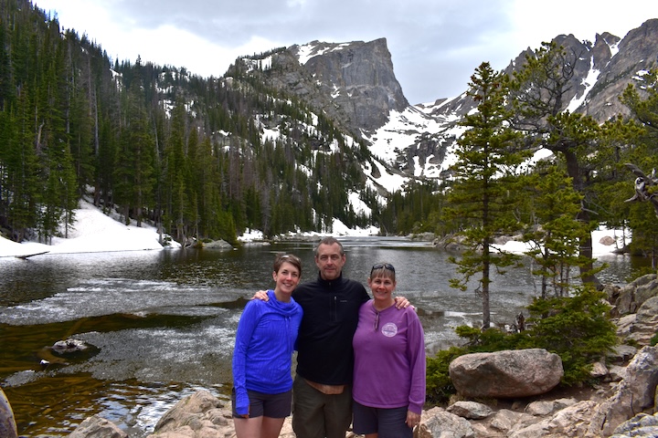 three people stand in front of Dream Lake in late spring