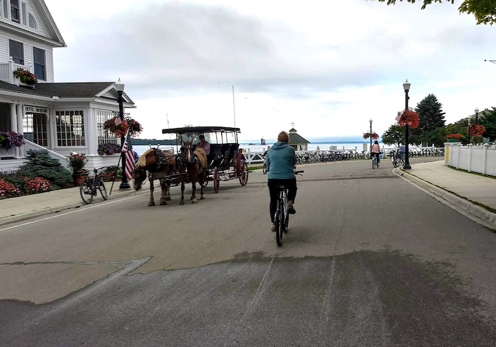 woman bikes the main street of Mackinac Island, horse-drawn wagon just to the left
