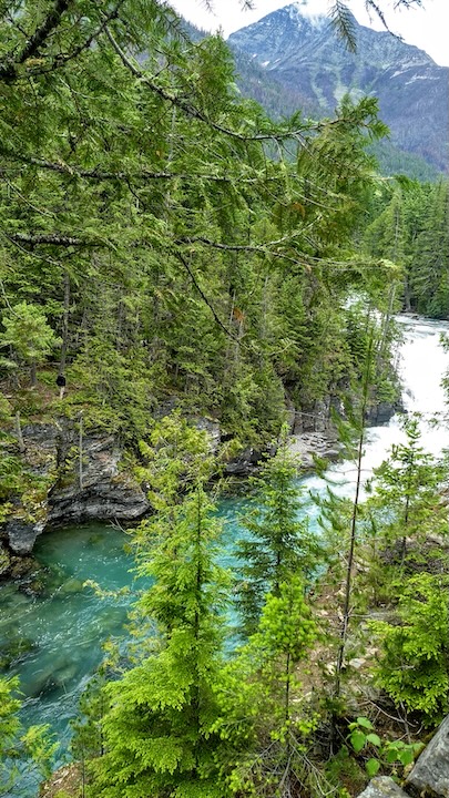 a clear, green river flows through a gorge with trees all around and a tall mountain in the background