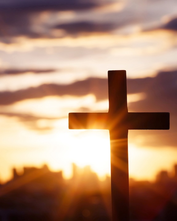 a wooden cross  stands before a sunset